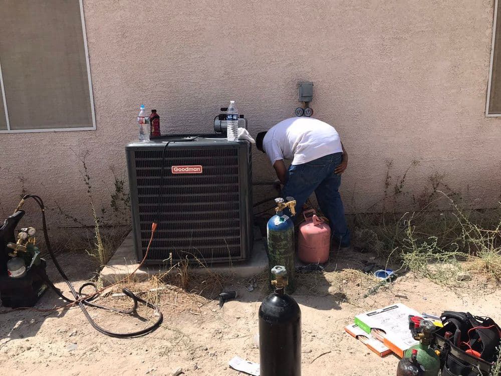 Technician servicing a Goodman air conditioning unit outdoors with tools and equipment.