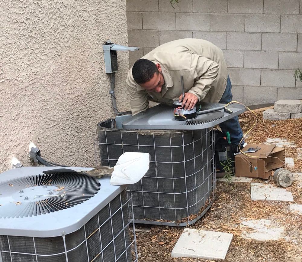 HVAC technician repairing an air conditioning unit in a backyard setting.