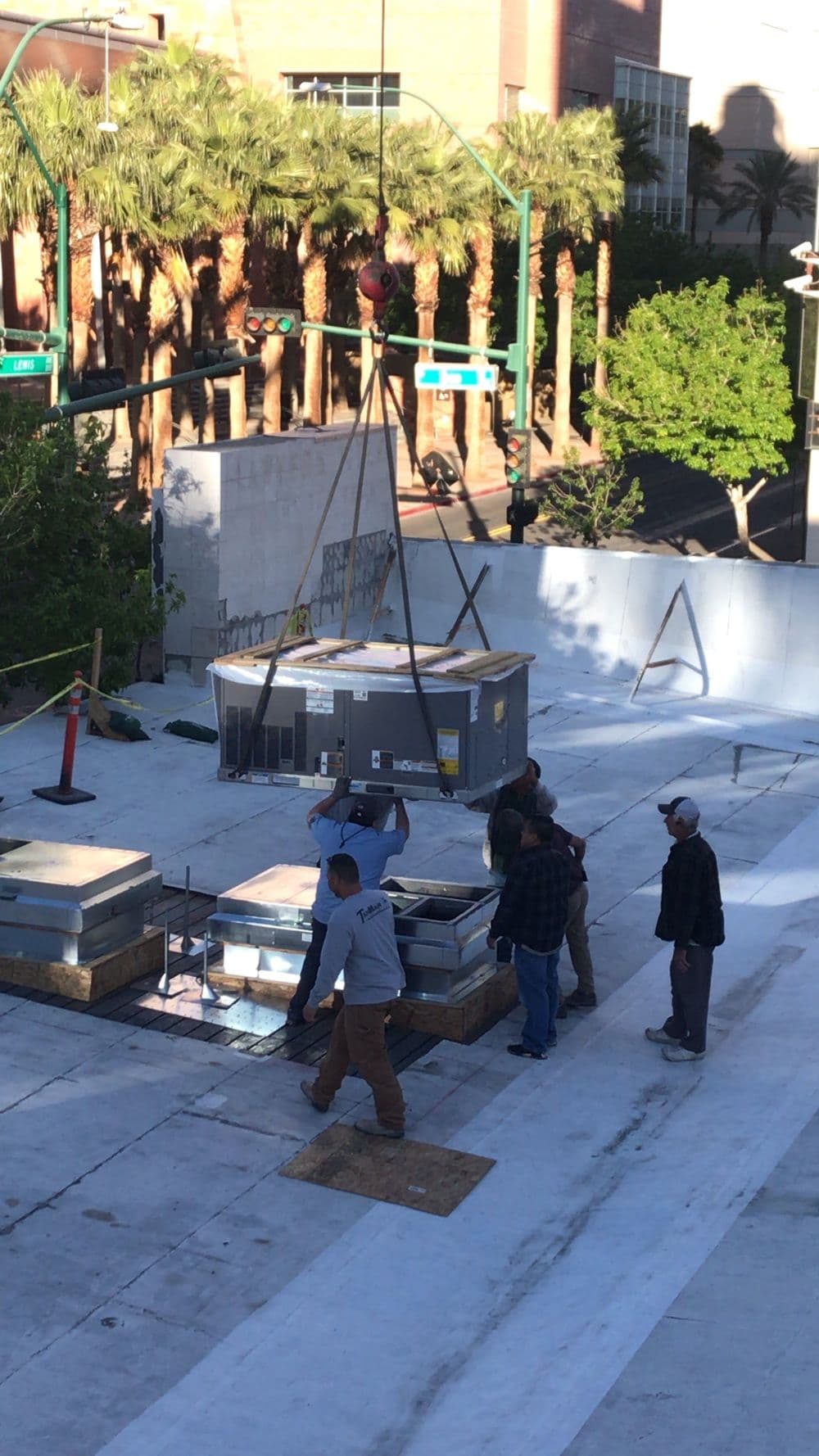 Workers installing HVAC units on a rooftop construction site with cranes and equipment.