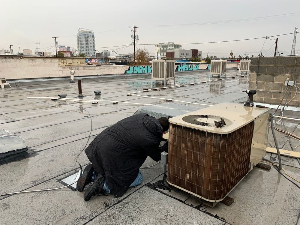 Technician servicing an HVAC unit on a commercial building rooftop.